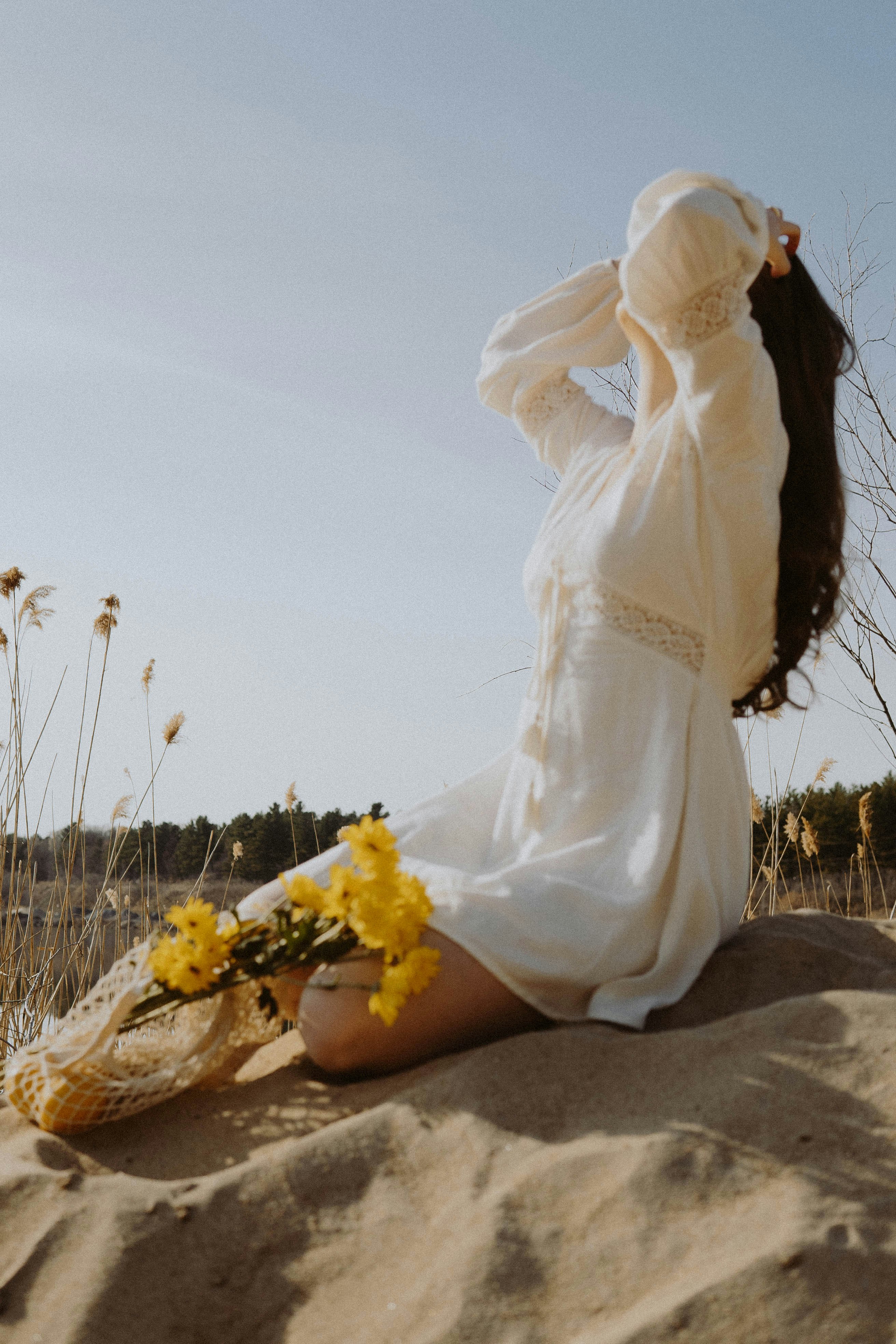 woman in white dress sitting on brown sand during daytime